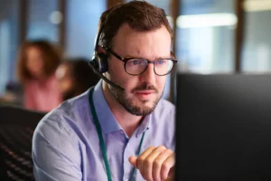 Focused man wearing glasses and headset working on a computer.