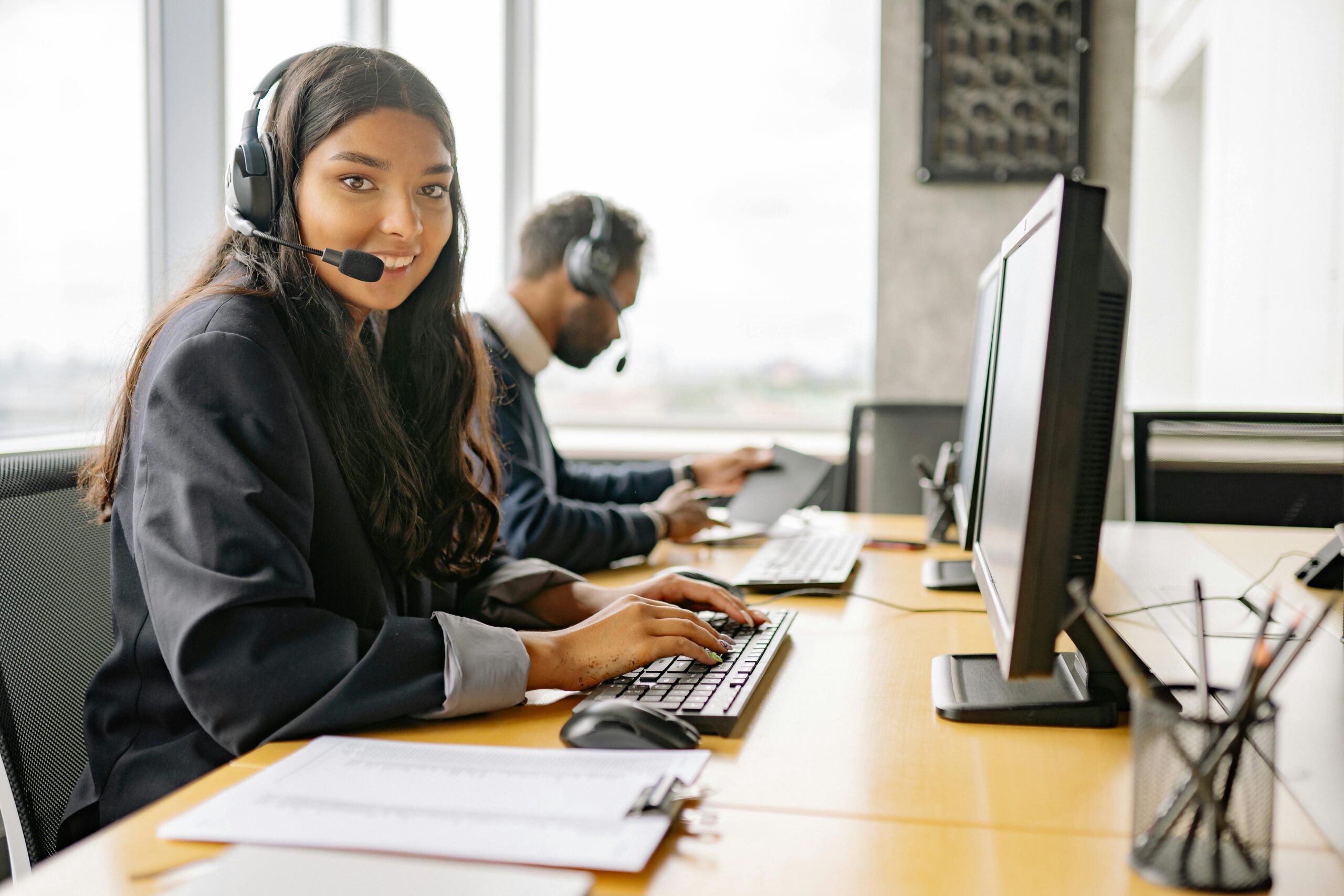 Woman at computer with headset, smiling.